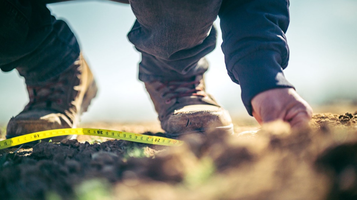 A close-up shot of a person using a measuring tape to determine the dimensions of a freshly laid gravel driveway.