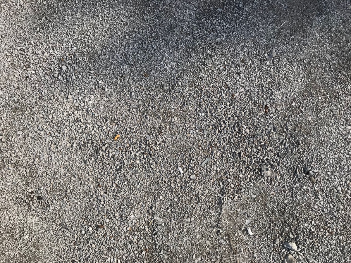 A large dump truck delivering a pile of crushed gravel onto a future driveway site.