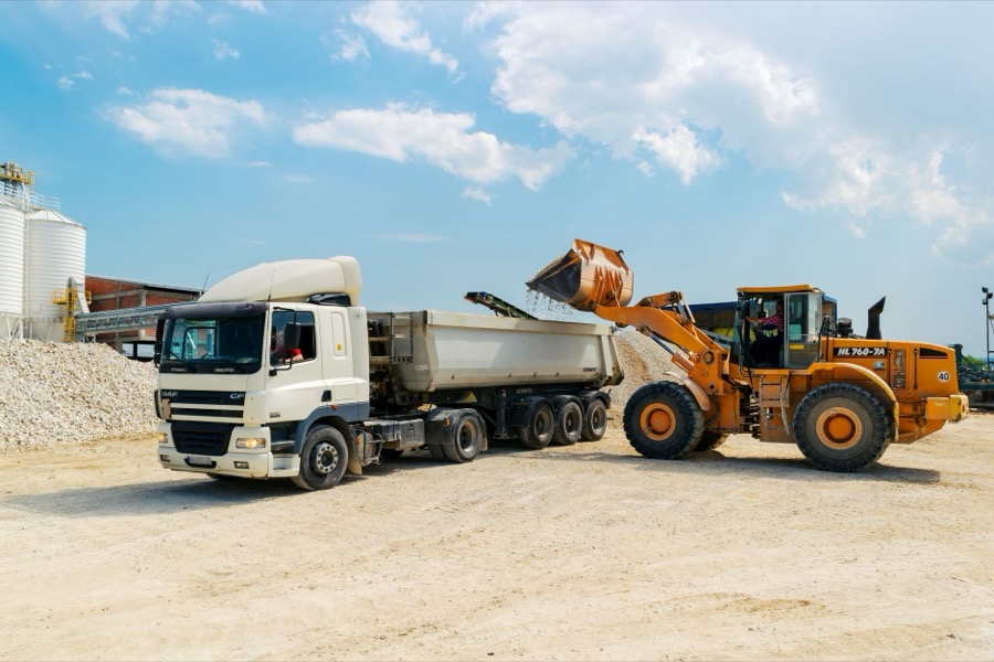 A large dump truck offloads a pile of crushed stone aggregate onto a residential construction site for a driveway.