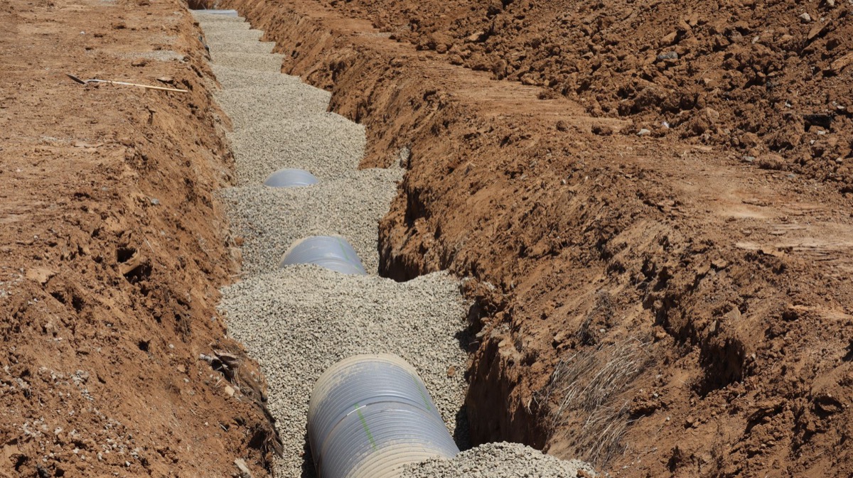 A professional crew installing a new gravel driveway on a residential property, with fresh stone and heavy equipment visible.