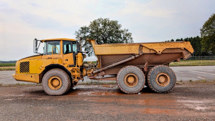 A large dump truck unloading crushed gravel aggregate onto a driveway construction site.