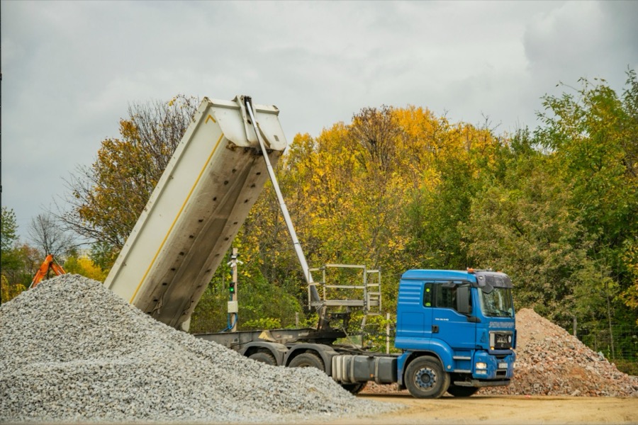 A large dump truck offloading a substantial pile of crushed stone aggregate onto a gravel driveway construction site.