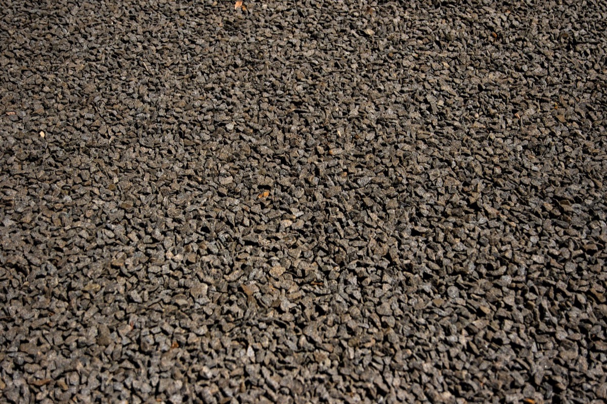 A newly installed gravel driveway, well-graded and smooth, leading towards a modern home, indicating a completed project.
