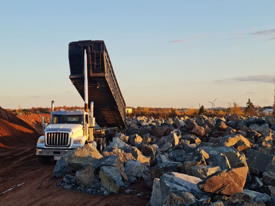 A large dump truck unloading crushed stone gravel onto a prepared driveway base.
