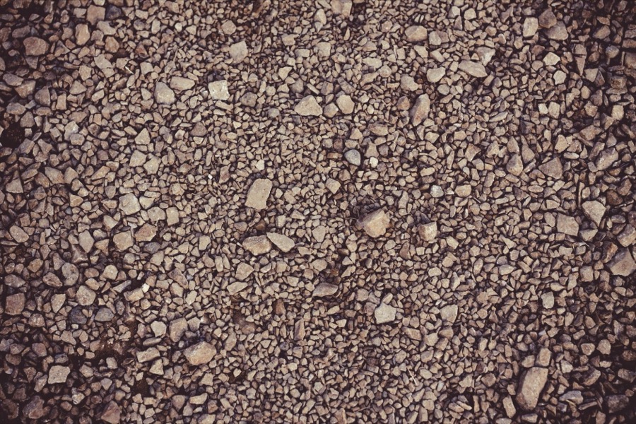 A cross-section or exposed view of compacted gravel driveway base layers, including geotextile fabric and different stone sizes.