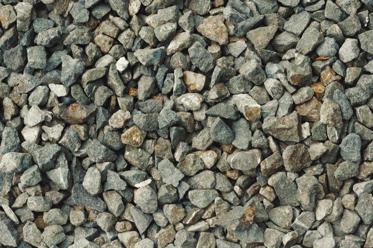 Fresh crushed stone spread across a gravel driveway with a rake nearby