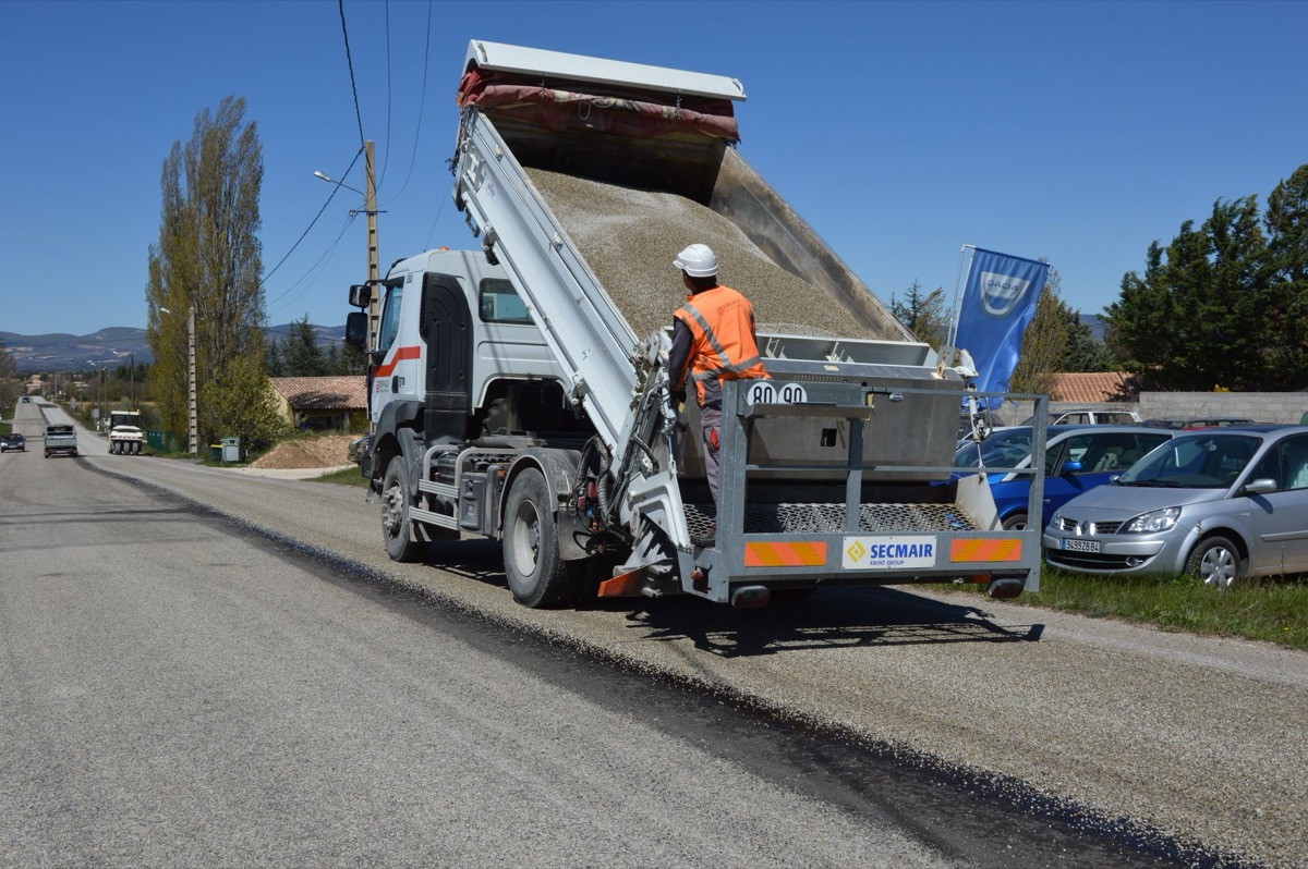 A large dump truck is unloading a pile of gravel onto a residential driveway under construction.